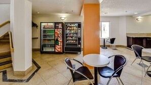 A hotel lobby with a staircase, vending machines, and a seating area with tables and chairs. - Motel 6 Katy, TX - Houston (Katy)