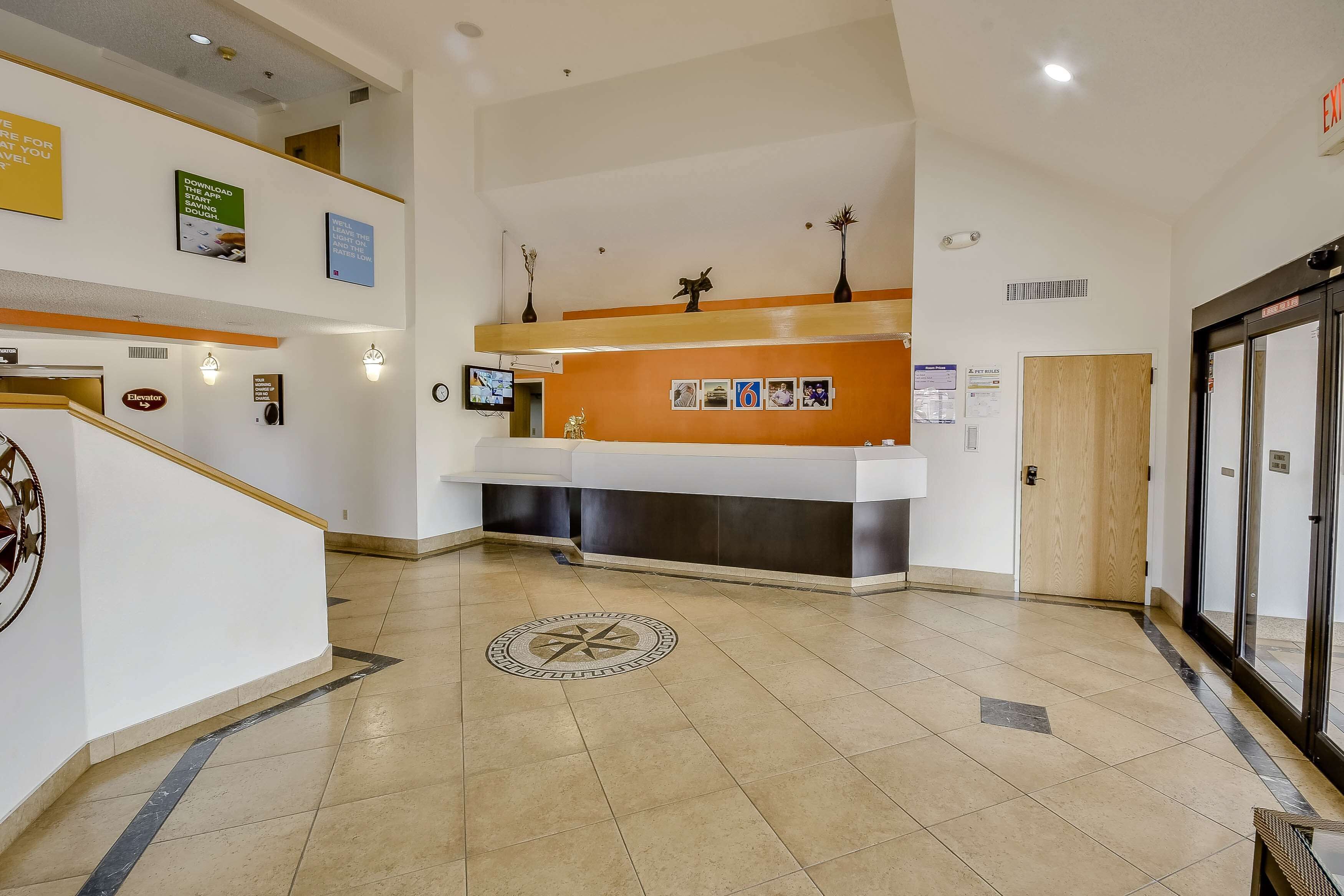 Un espace d’accueil d’hôtel au design moderne, comprenant un comptoir d’accueil, un écran numérique et un escalier.