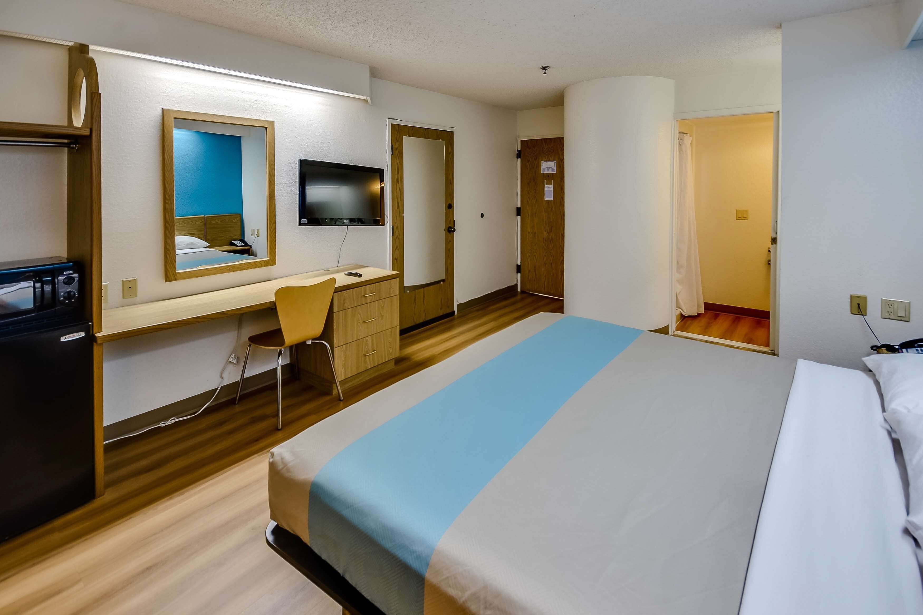 Una habitación de hotel con cama, escritorio, silla, televisor y armario.