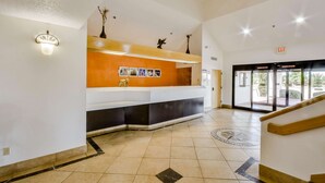 A reception area with a counter, a wall-mounted light fixture, and a door leading outside. - Motel 6 Katy, TX - Houston (Katy)