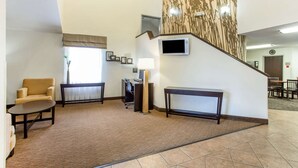 A hotel lobby with a carpeted floor, a sofa, a desk with a computer, a TV mounted on the wall, and a staircase leading to another area. - Sleep Inn Provo near University (Provo)