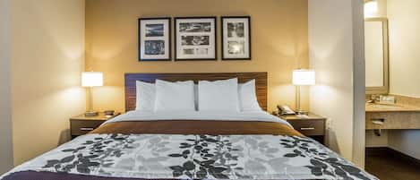 A hotel room with a bed, two bedside tables, a nightstand, a mirror, and a framed photo collage on the wall.