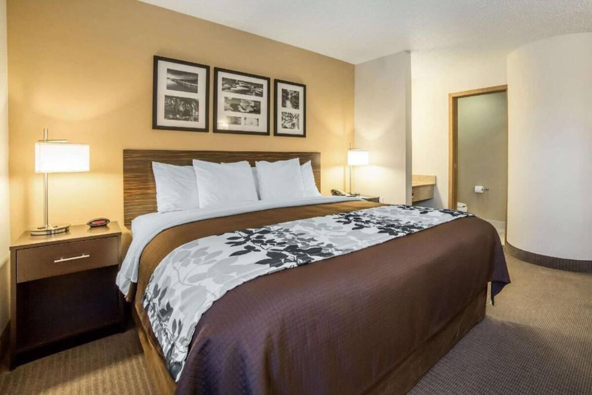 Habitación de hotel con cama, mesitas de noche, lámparas, una puerta y cuadros en la pared.