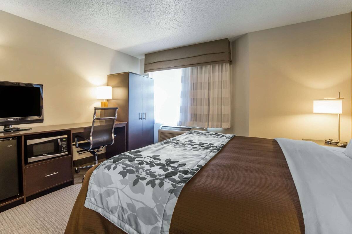 Una habitación de hotel con cama, escritorio, televisor, microondas y una silla.