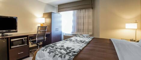 A hotel room with a bed, a desk with a television, a microwave, and a chair.
