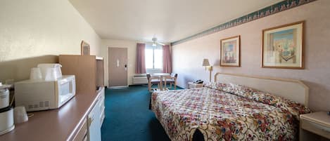 A hotel room with a bed, a desk, a chair, a microwave, and a small table.