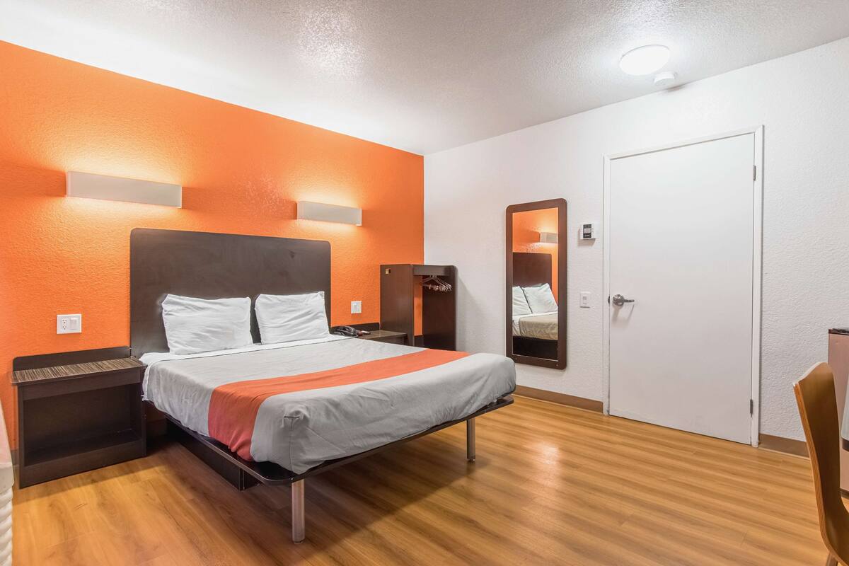 Quarto de hotel com cama, mesas de cabeceira, espelho, guarda-roupa e porta.