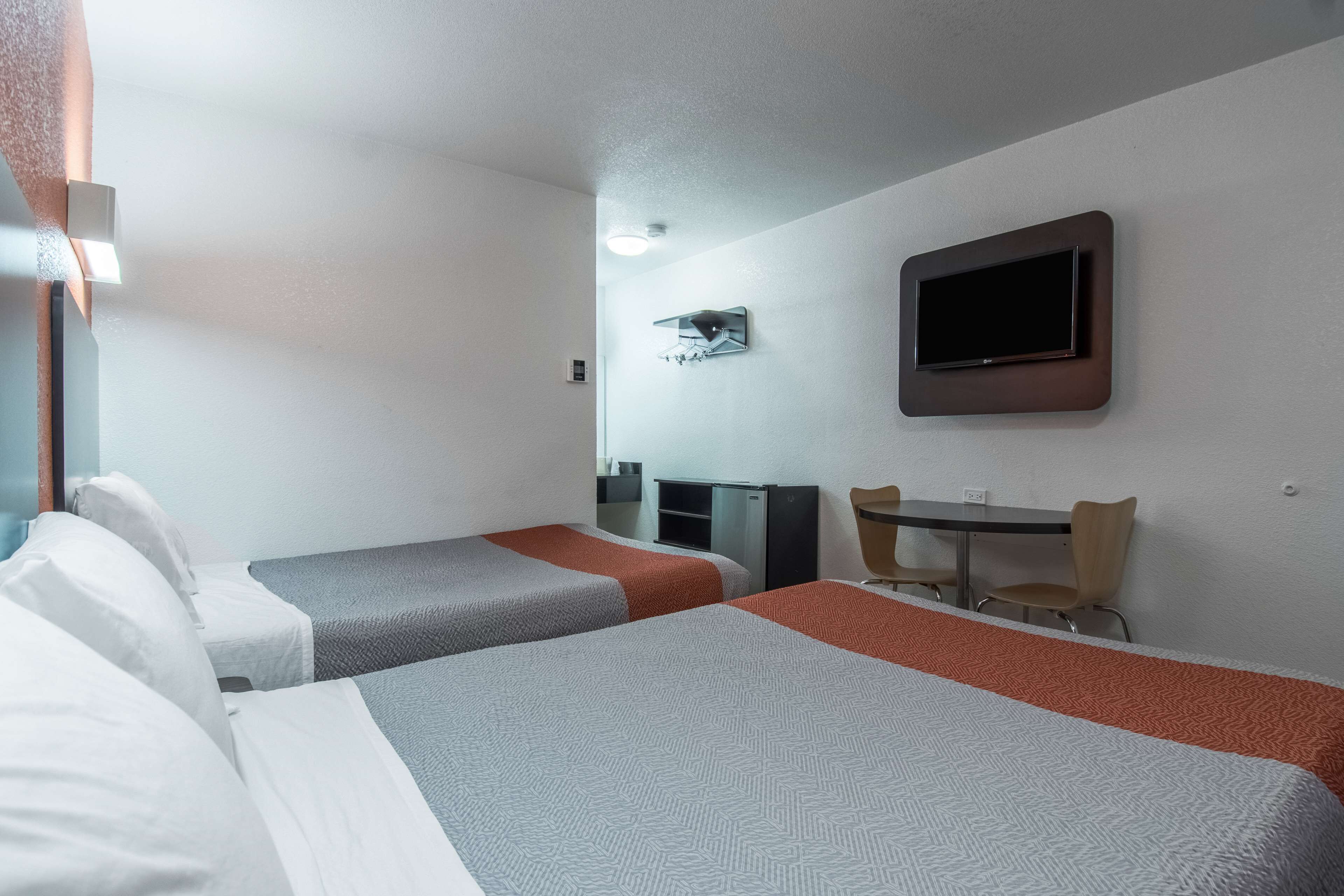 A hotel room with two beds, a desk, a chair, a TV, and a small table.