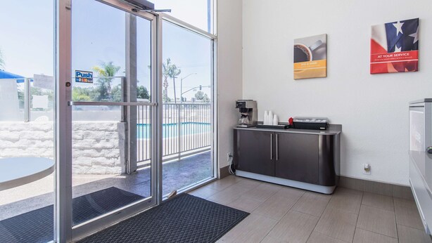 A hotel lobby with a sliding glass door, a reception desk, a coffee machine, and two framed pictures on the wall. - Motel 6 Bakersfield, CA - Central (Bakersfield)
