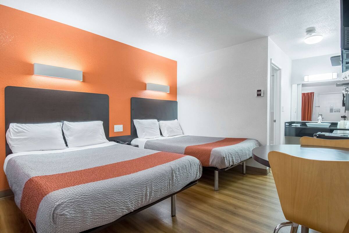 Quarto de hotel com duas camas, uma mesa de jantar de madeira e uma pequena cozinha.