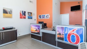 A hotel reception area with a modern design, featuring a reception desk, a flat-screen TV, and a digital display board. - Motel 6 Bakersfield, CA - Central (Bakersfield)