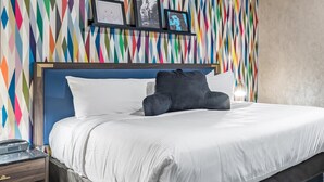 A hotel room with a bed, a nightstand, a wall with colorful geometric patterns, and framed pictures. - Signature Inn Merced Yosemite Parkway (Merced)