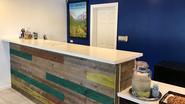 A reception desk with a colorful wooden panel design, a poster of Yosemite National Park, a white door, and a small table with a water dispenser and snacks. - Signature Inn Merced Yosemite Parkway (Merced)