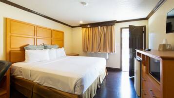 A hotel room with a large bed, a desk with a television, and an air conditioning unit.