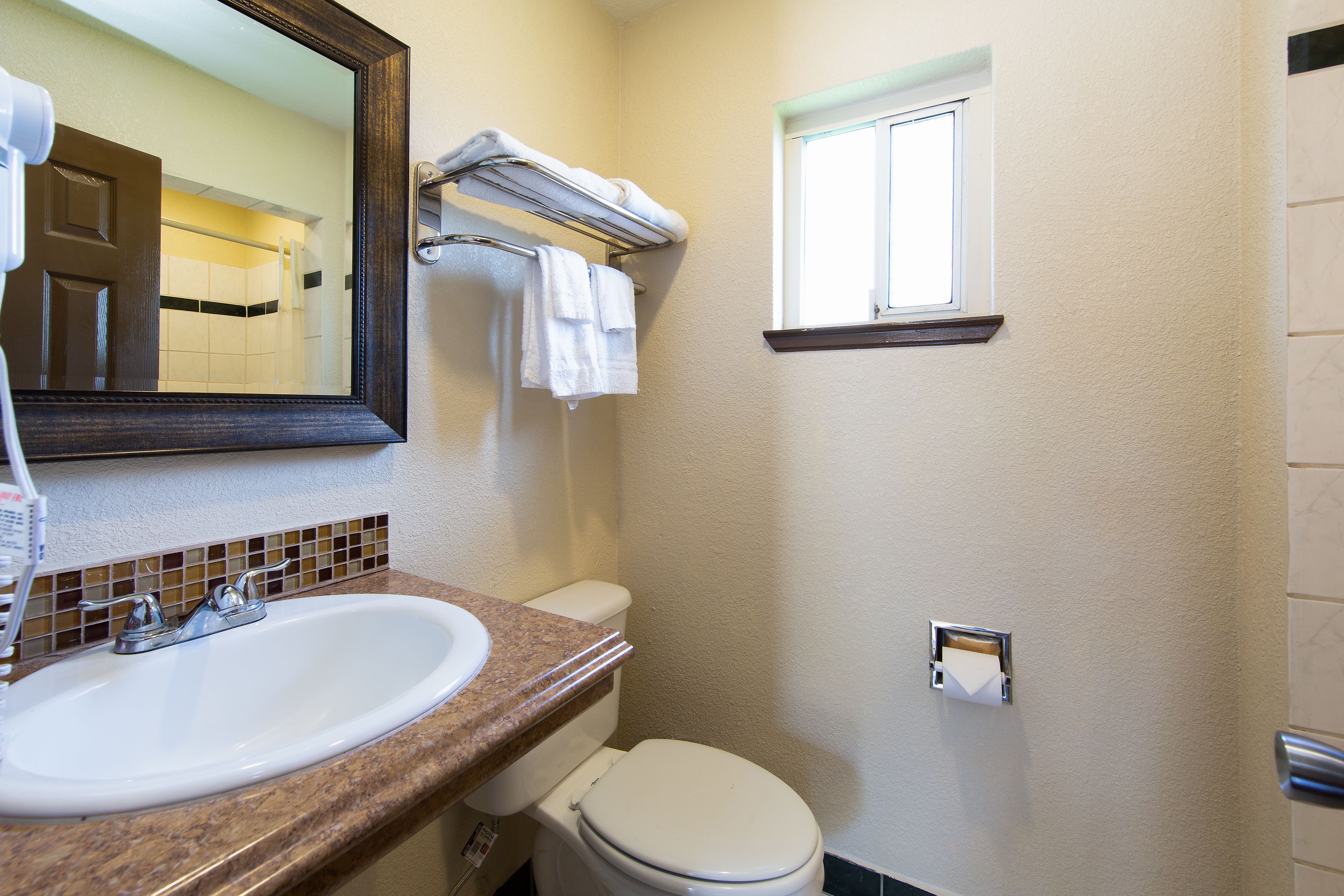 Un baño con lavamanos, espejo, toallero, inodoro y ventana.
