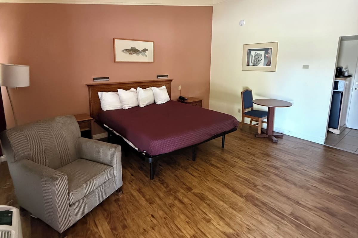 A bedroom with a bed, a chair, a small table, and a desk.