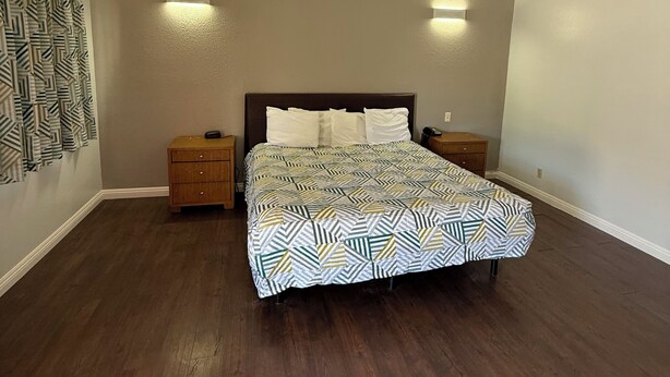 A bedroom with a bed, two nightstands, a patterned bedspread, wooden nightstands, and a ceiling with exposed beams.
