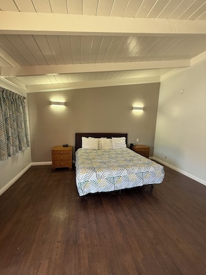 Un dormitorio con una cama, dos mesitas de noche, una colcha estampada, mesitas de noche de madera y un techo con vigas a la vista.