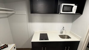 A compact kitchen with a microwave, sink, and cabinets. - Oroville Value Suites (Oroville)