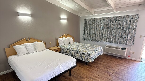 A bedroom with two beds, wooden flooring, a ceiling fan, and a patterned curtain. - Oroville Value Suites (Oroville)
