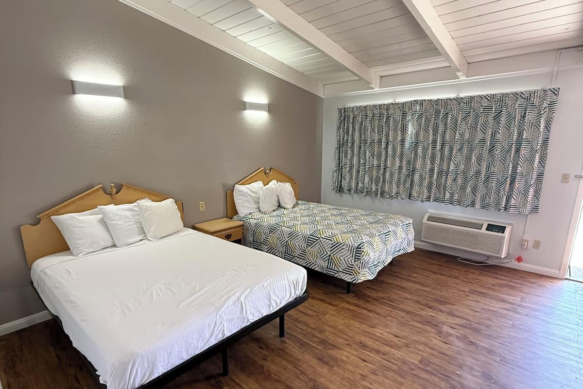 A bedroom with two beds, wooden flooring, a ceiling fan, and a patterned curtain.