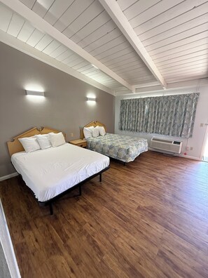 Un dormitorio con dos camas, suelo de madera, ventilador de techo y cortina estampada.