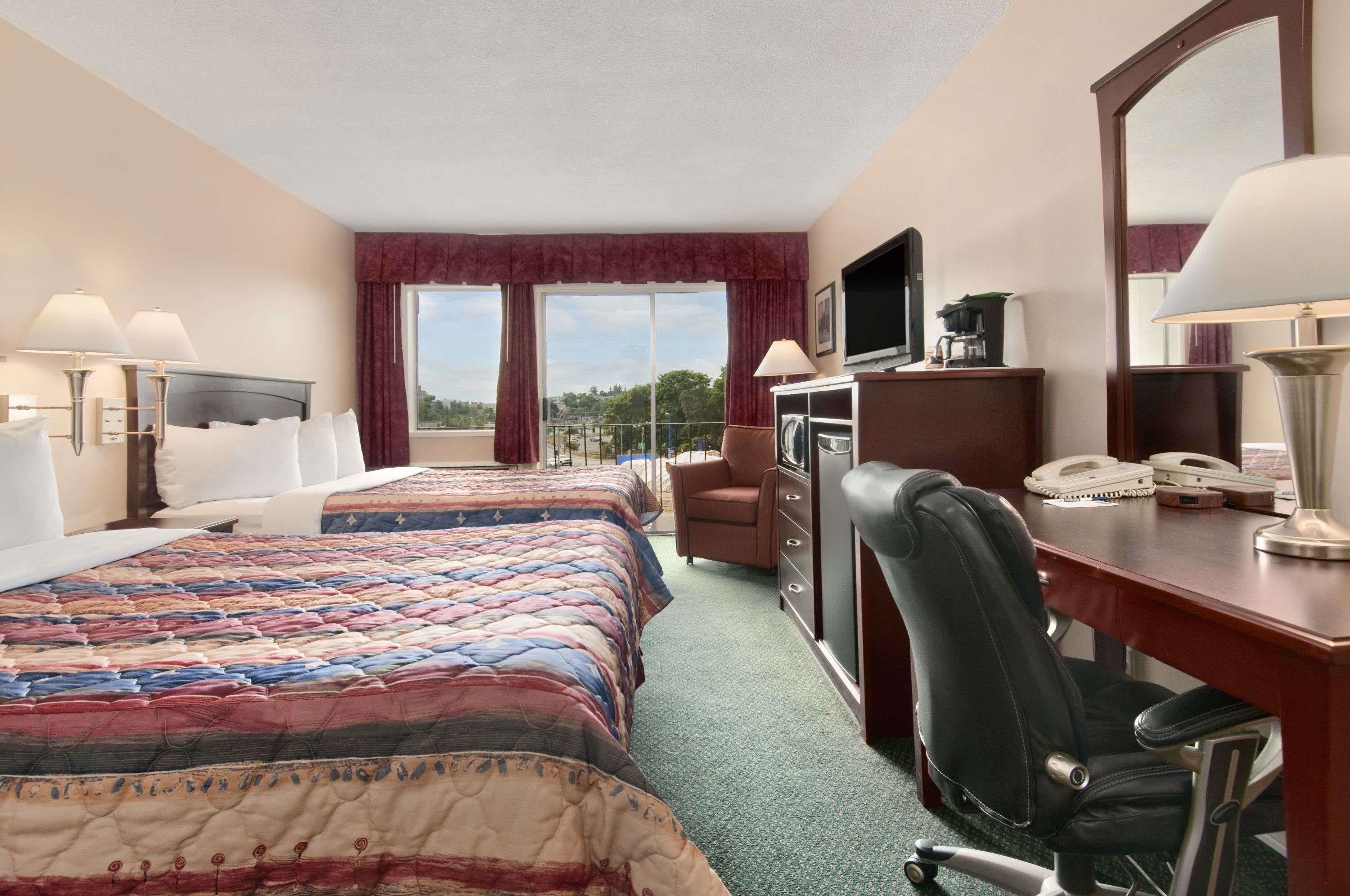 A hotel room with two beds, a desk, a chair, a television, and a large window offering a view.