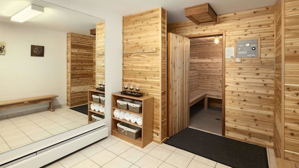 Un cuarto de sauna con paredes de madera, un banco y repisas con toallas y cristalería.