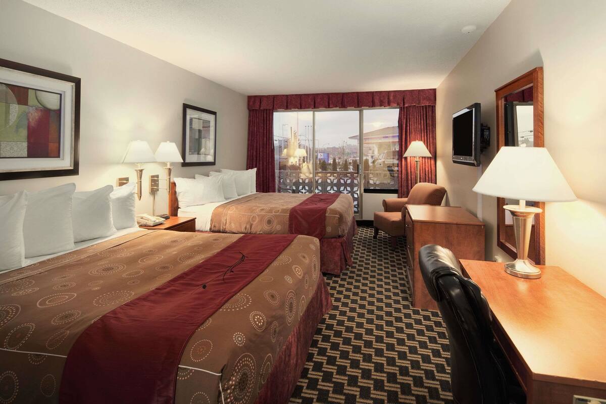 A hotel room with two beds, a desk, a chair, a TV, and a large window with a view.