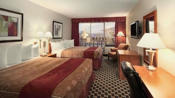 Ein Hotelzimmer mit zwei Betten, einem Schreibtisch, einem Stuhl, einem Fernseher und einem großen Fenster mit Blick.