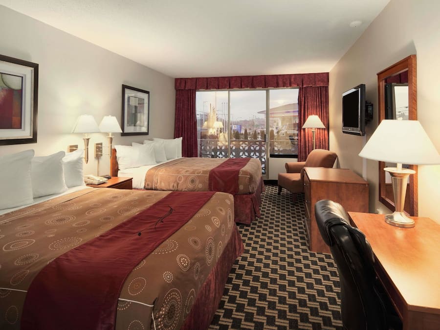 Une chambre d’hôtel avec deux lits, un bureau, une chaise, une télévision et une grande fenêtre donnant sur un beau paysage.