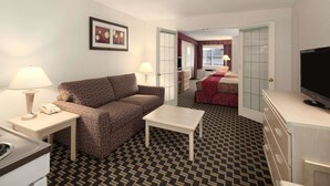 Habitación de hotel con alfombra estampada, un sofá, una mesita, un televisor y una kitchenette.