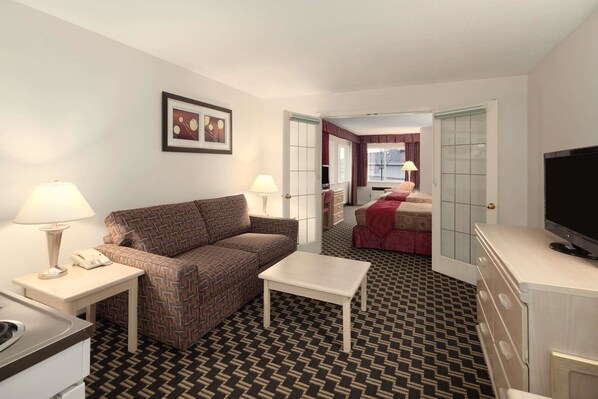 A hotel room with a patterned carpet, a sofa, a small table, a TV, and a kitchenette.