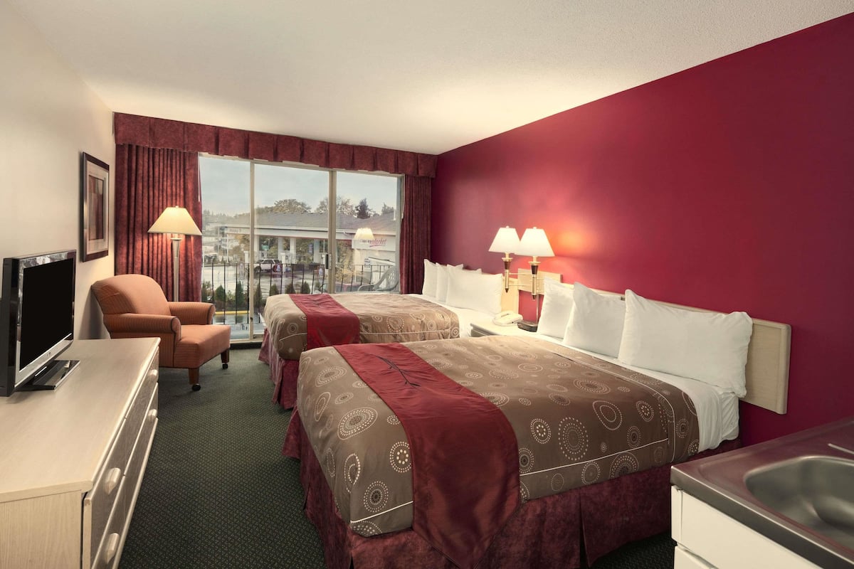A hotel room with two beds, a desk, a chair, and a TV.