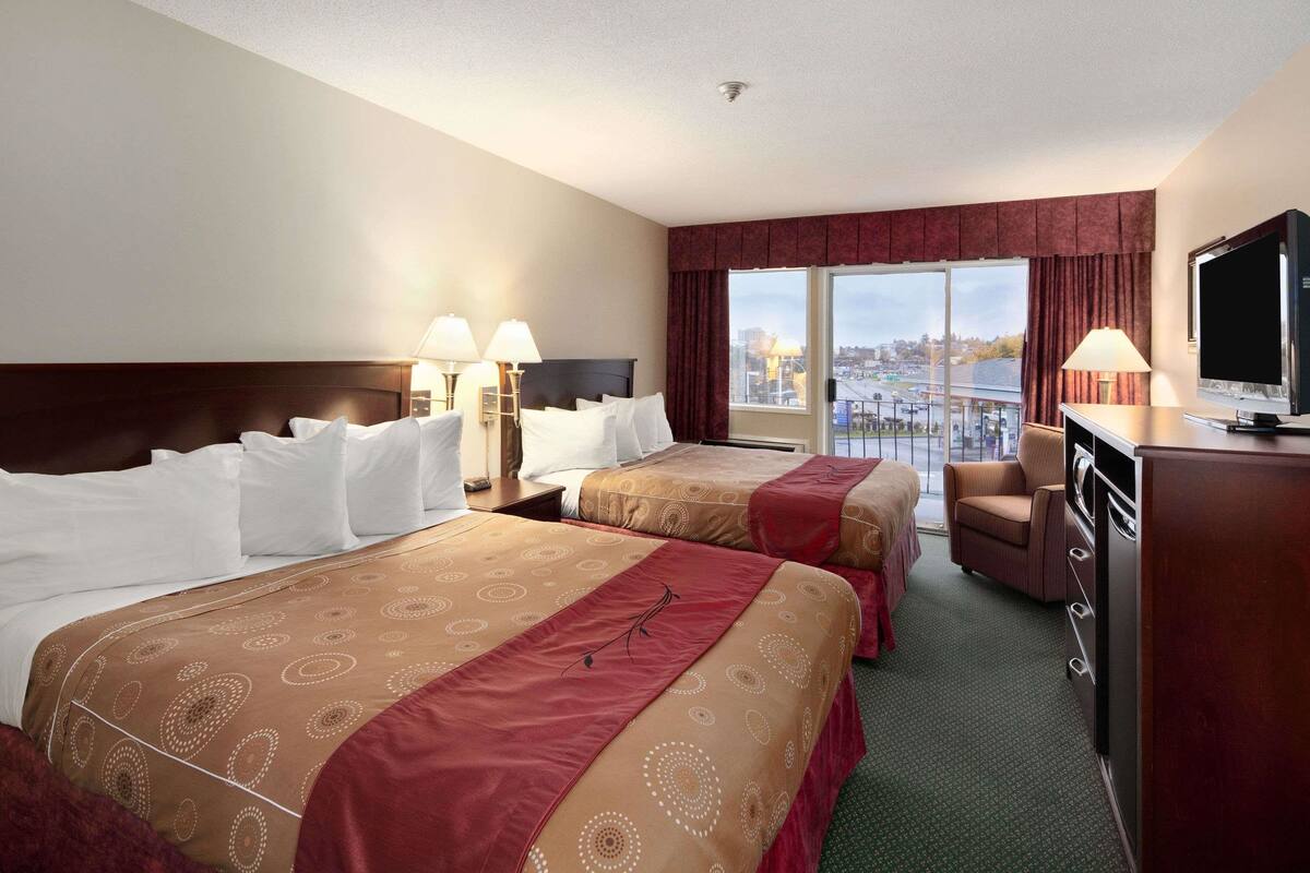 A hotel room with two beds, a television, a desk, and a view of the city.