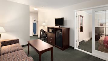 Ein Hotelzimmer mit einer Couch, einem Holztisch, einem Fernseher auf einem Schrank, einem Schreibtisch mit Stuhl und einer Glastür zu einem Balkon.