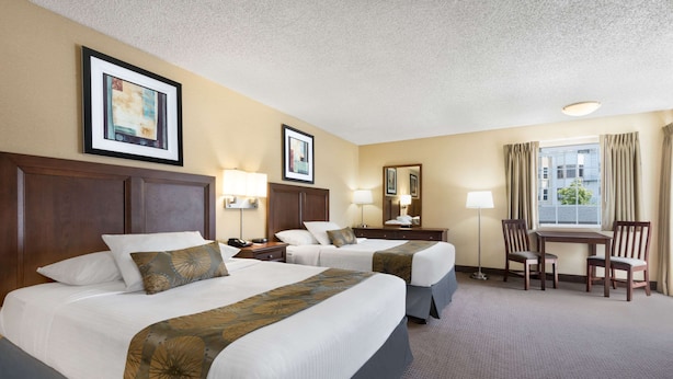 A hotel room with two beds, a desk, chairs, and a window with curtains.