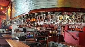 A bar area with a curved counter, multiple stools, and a variety of bottles and glasses.