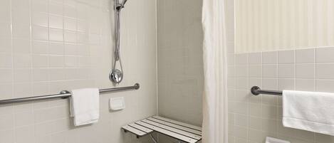 A shower area with a handheld showerhead, a grab bar, a bench, and a towel rack.