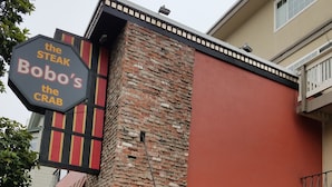 A brick building with a striped awning and a sign that reads "the STEAK Bobo's the CRAB".