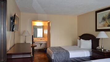Hotelkamer met twee bedden, een bureau, een stoel, een lamp, een schilderij en een badkamer zichtbaar door een geopende deur.