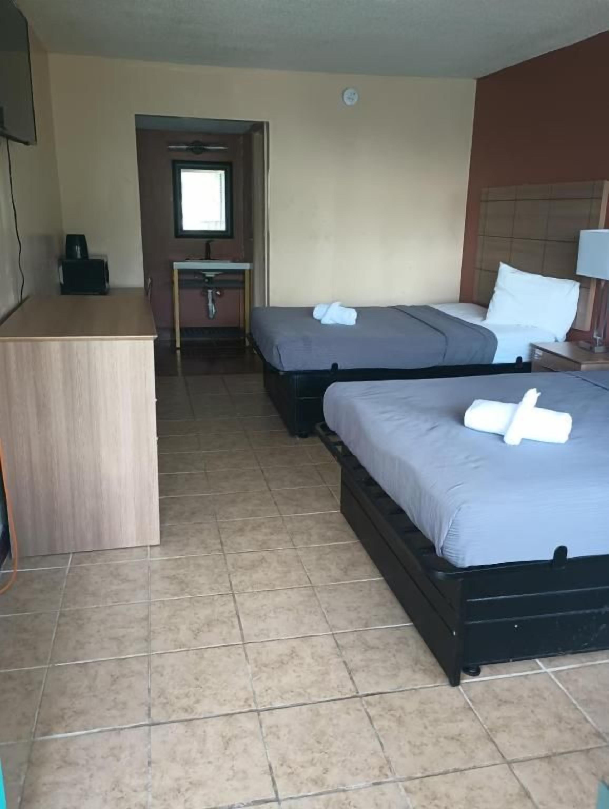 A hotel room with two beds, a desk, a mirror, and a window.