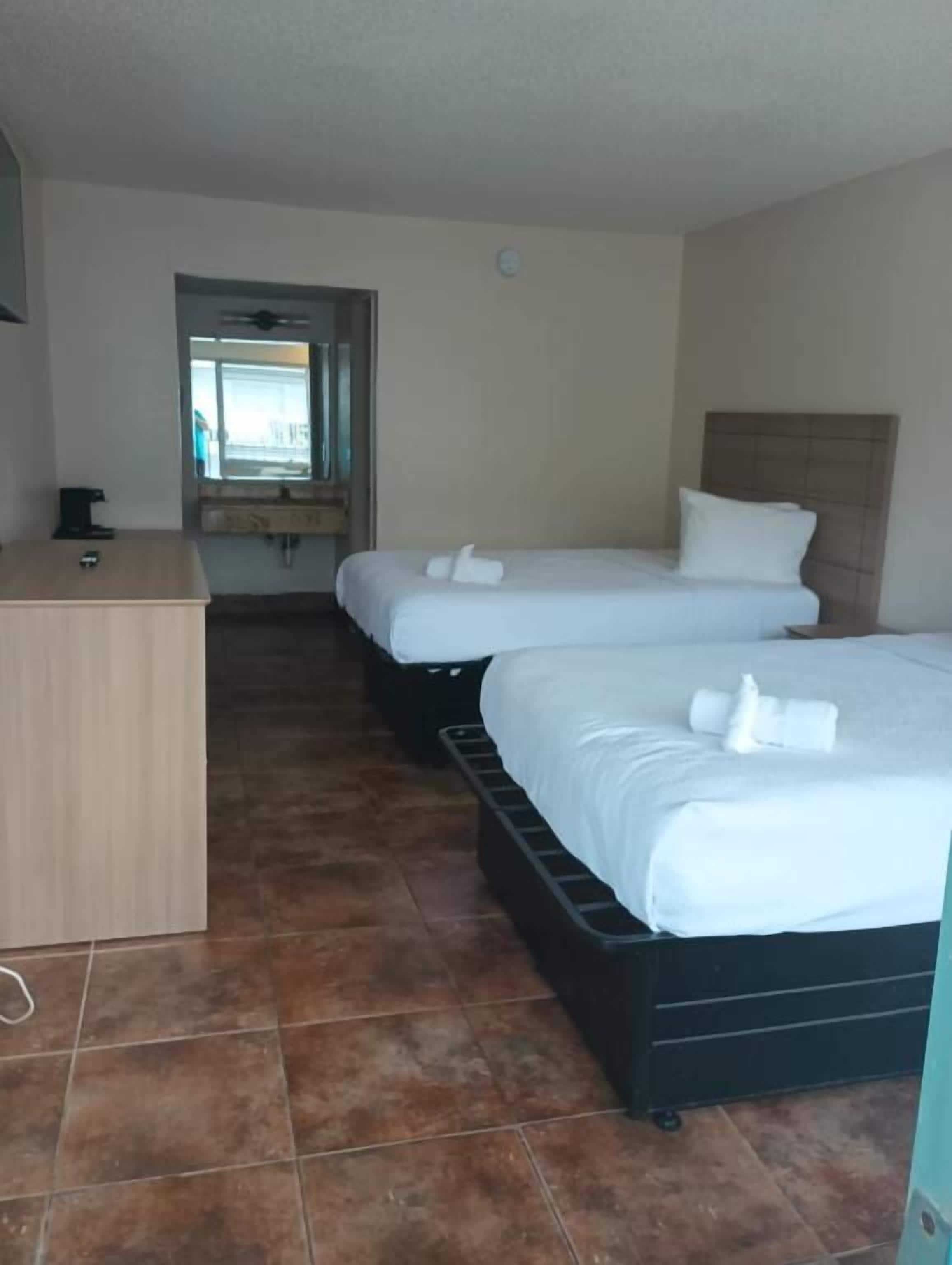 A hotel room with two beds, a desk, and a window.