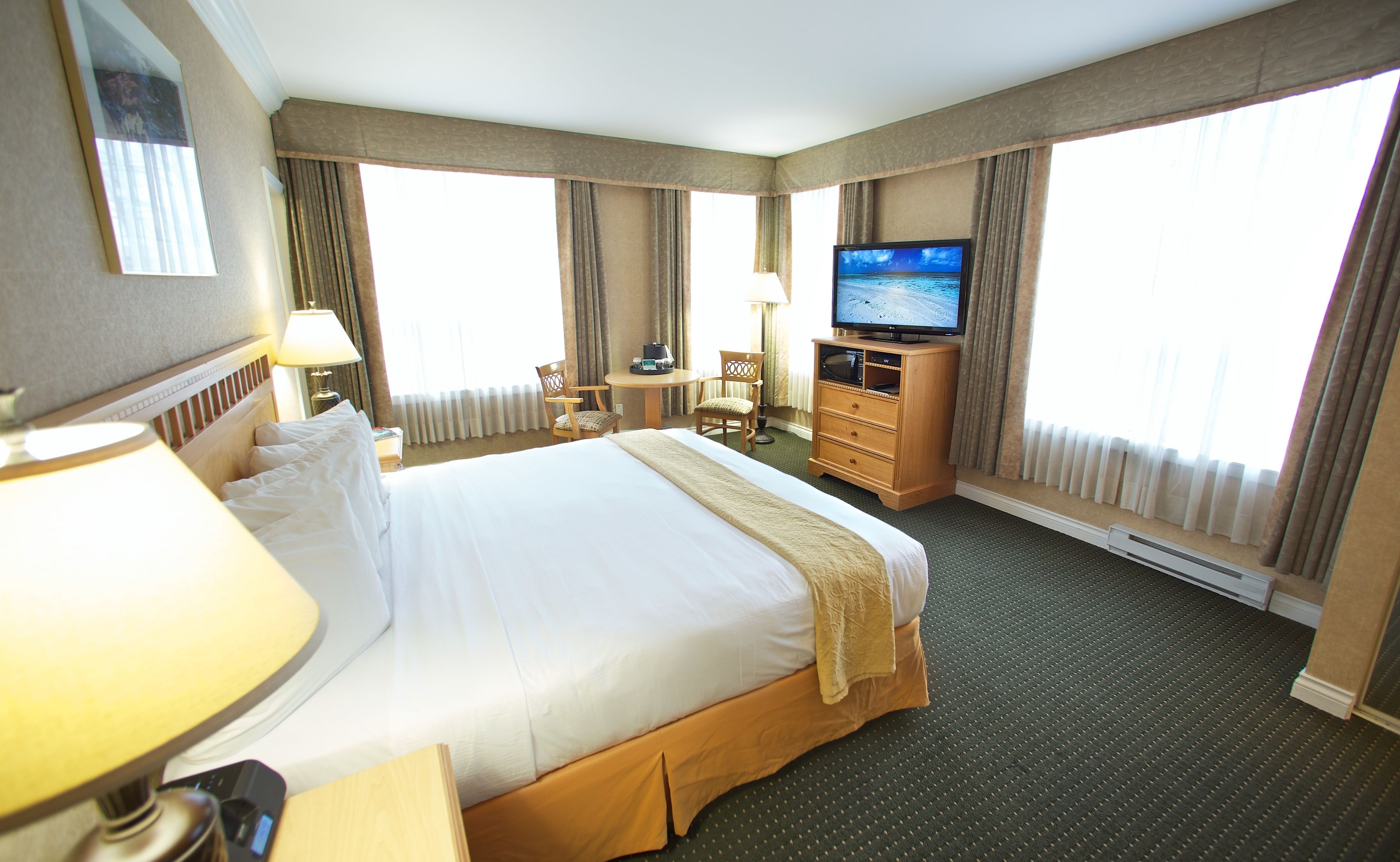 Quarto de hotel com uma cama grande, televisão, escrivaninha com candeeiro e uma cadeira.