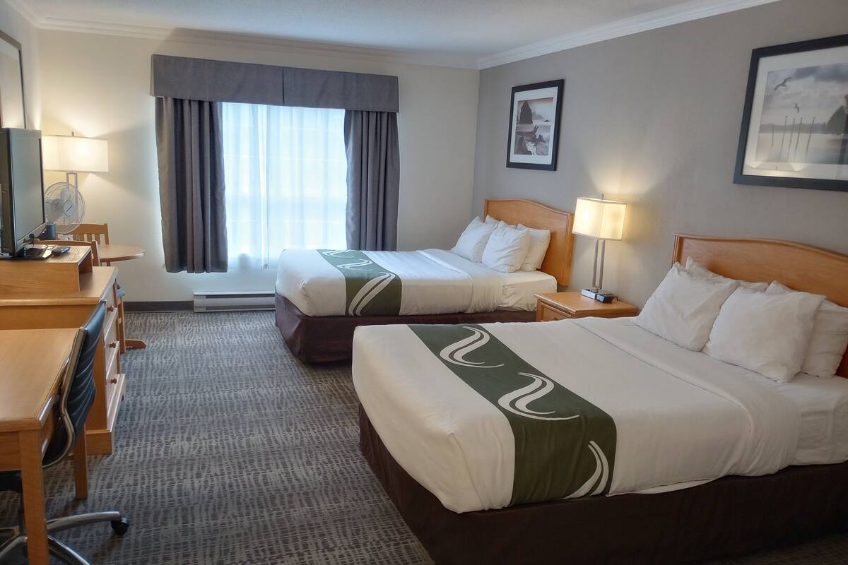 Een hotelkamer met twee bedden, een bureau, een stoel, een lamp en een raam met gordijnen.