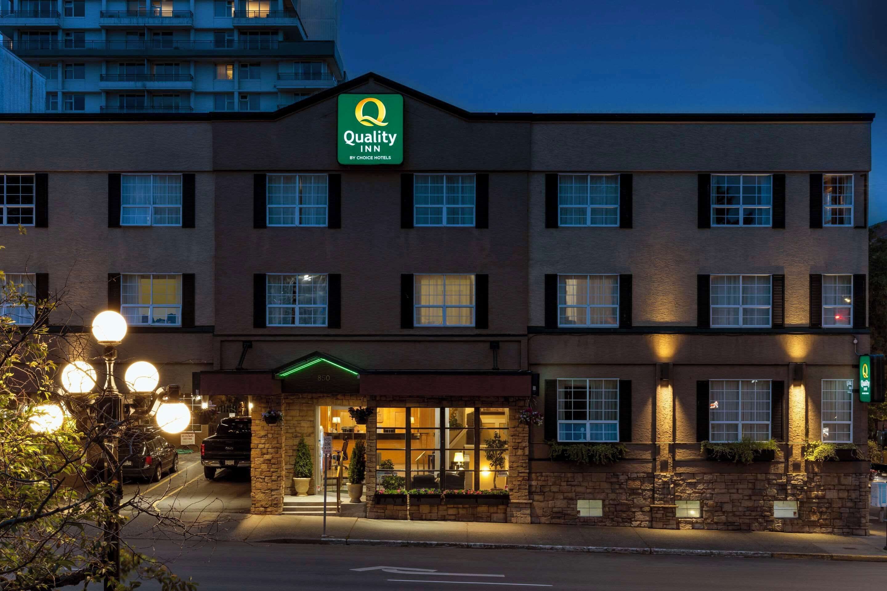 A hotel with a sign reading "Quality Inn by Choice Hotels." It features a brick facade, multiple windows, and a well-lit entrance.