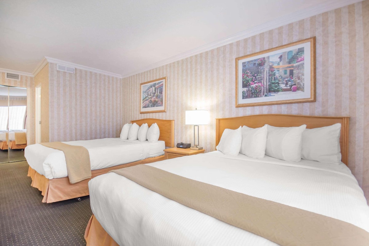 A hotel room with two beds, a nightstand with a lamp, and two framed pictures on the wall.