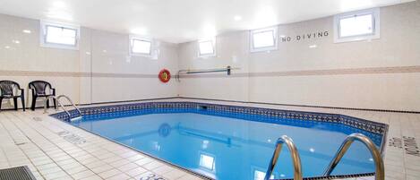 Una piscina interior con agua cristalina, suelo de baldosas marcado con medidas de profundidad y señalización de seguridad.