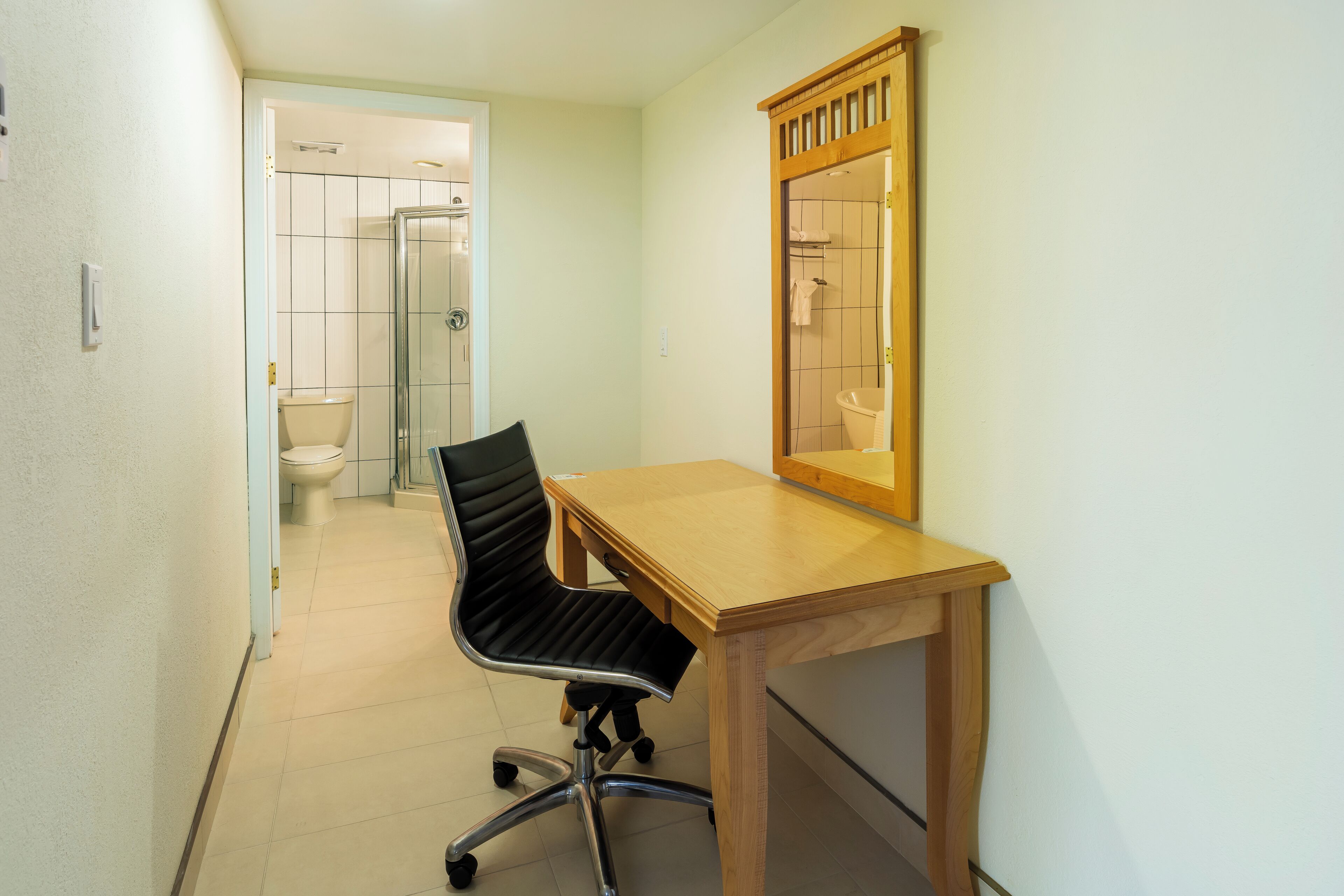 A small, narrow bathroom with a toilet, a shower, and a wooden desk with a chair.