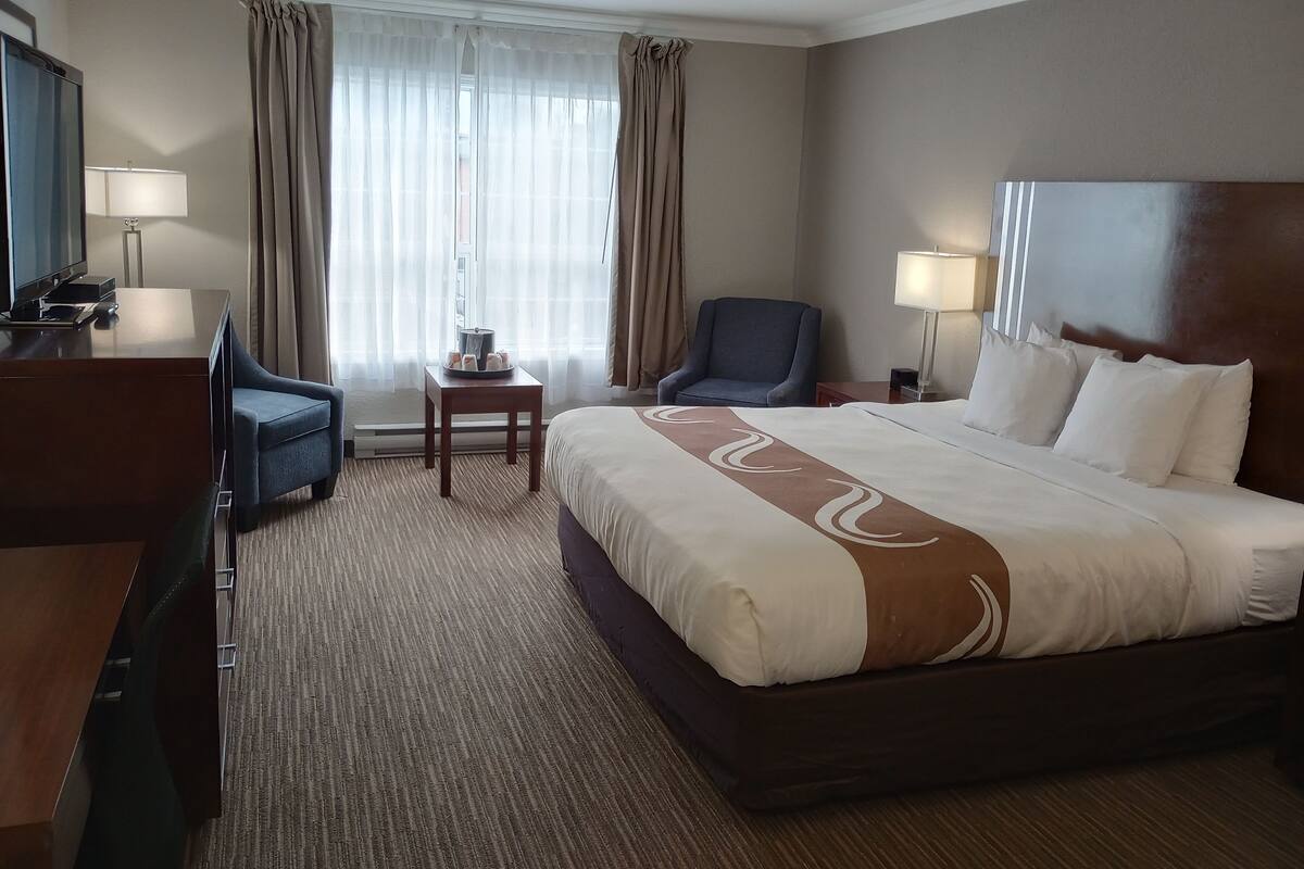 Een hotelkamer met een groot bed, een bureau met een computer, een stoel, een klein tafeltje met een schaal snacks en een televisie.
